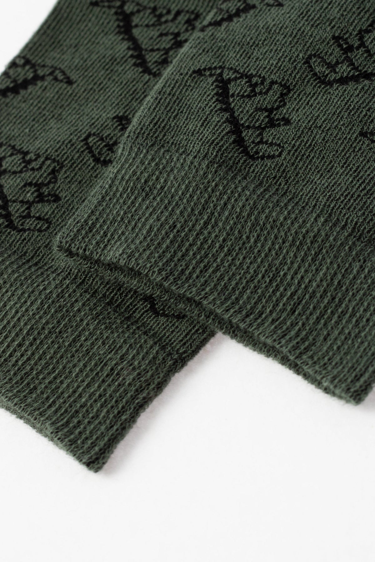 A close-up view of two dark green ribbed cuffs with an all-over black dinosaur pattern.