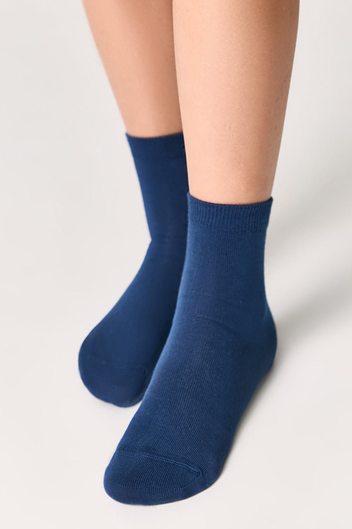 A pair of mid-calf socks in a solid dark blue color are worn on a person's feet against a light grey background.