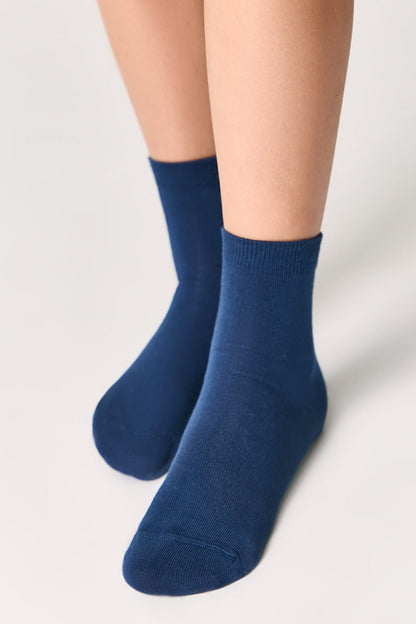 A pair of mid-calf socks in a solid dark blue color are worn on a person's feet against a light grey background.