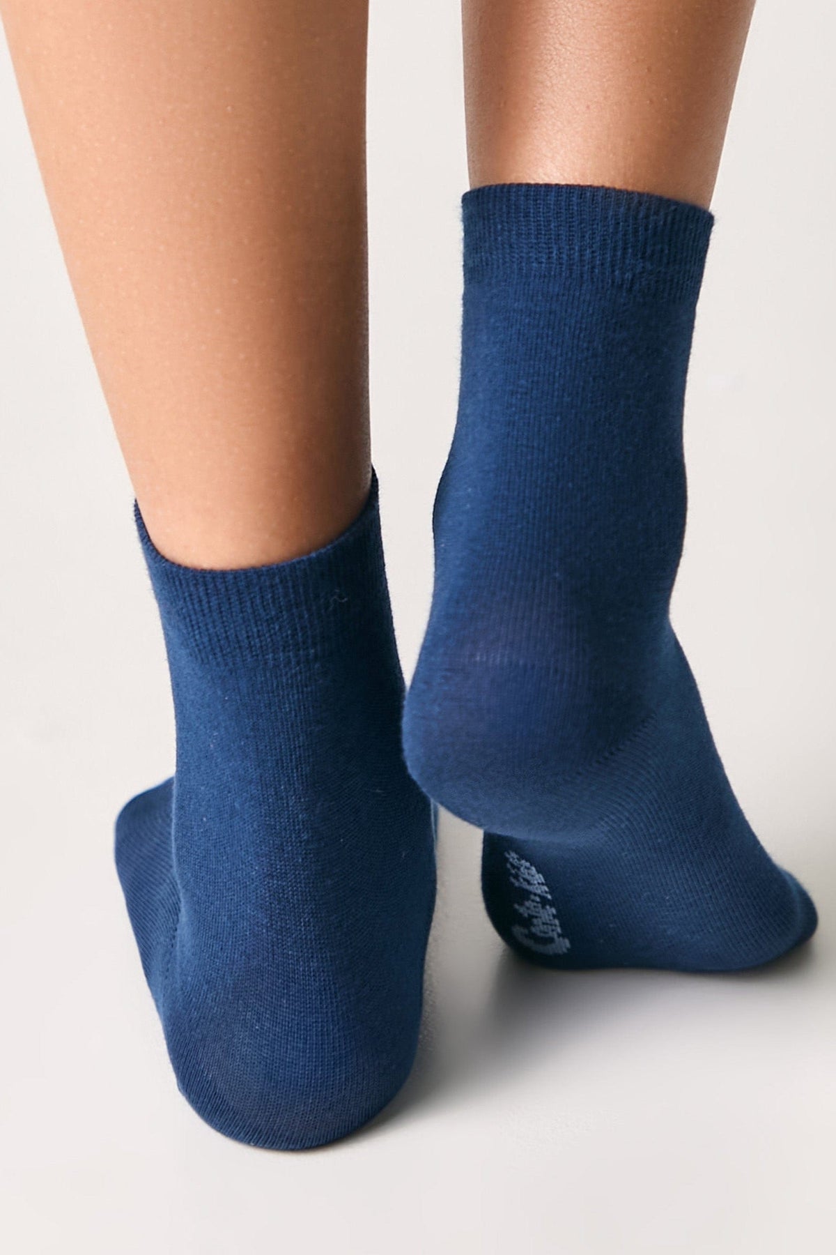 A pair of mid-calf socks in a solid dark blue color are worn on a person's feet against a plain white background.