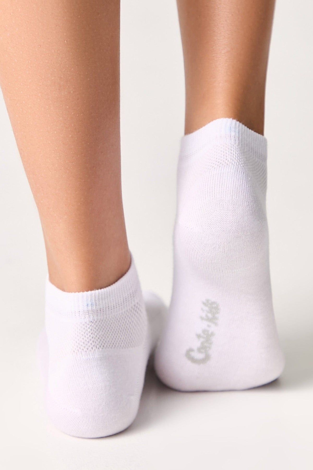 A pair of white ankle socks worn on the feet, featuring a small grey brand logo printed on the back of the heel.