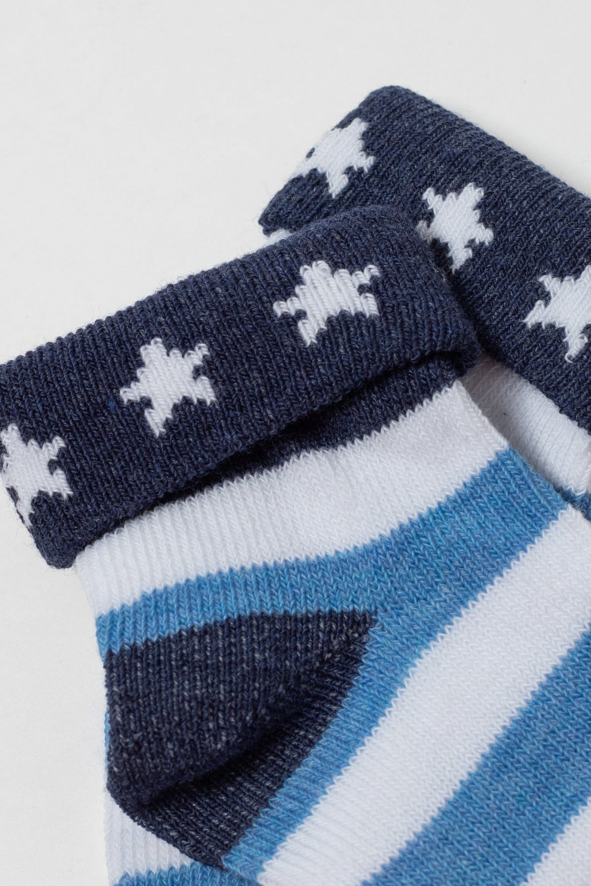 A pair of baby socks featuring white star patterns on a dark blue ribbed cuff and blue and white horizontal stripes on the feet.
