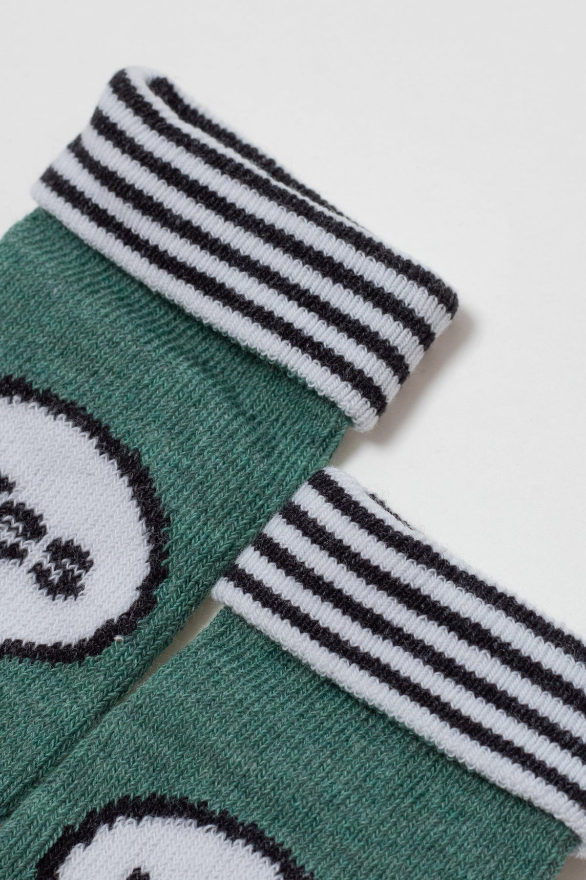 A pair of green ribbed-knit ankle socks featuring a white and black striped cuff and a partially visible white graphic on the leg.