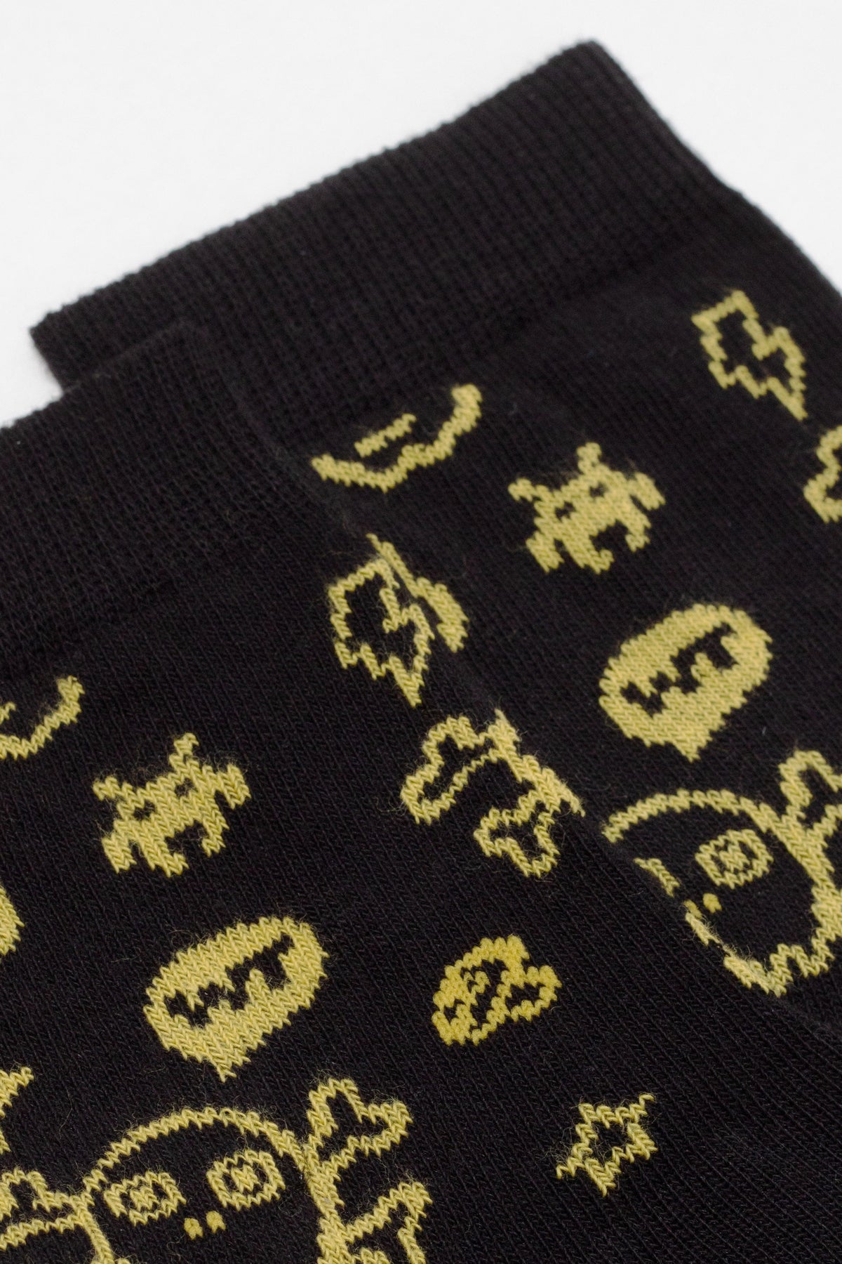 A close-up view of black socks featuring a repeating pattern of yellow, retro-style pixelated skull and star icons.