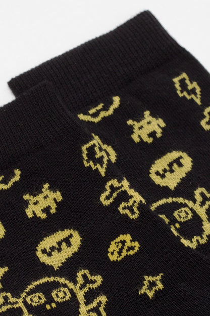A close-up view of black socks featuring a repeating pattern of yellow, retro-style pixelated skull and star icons.