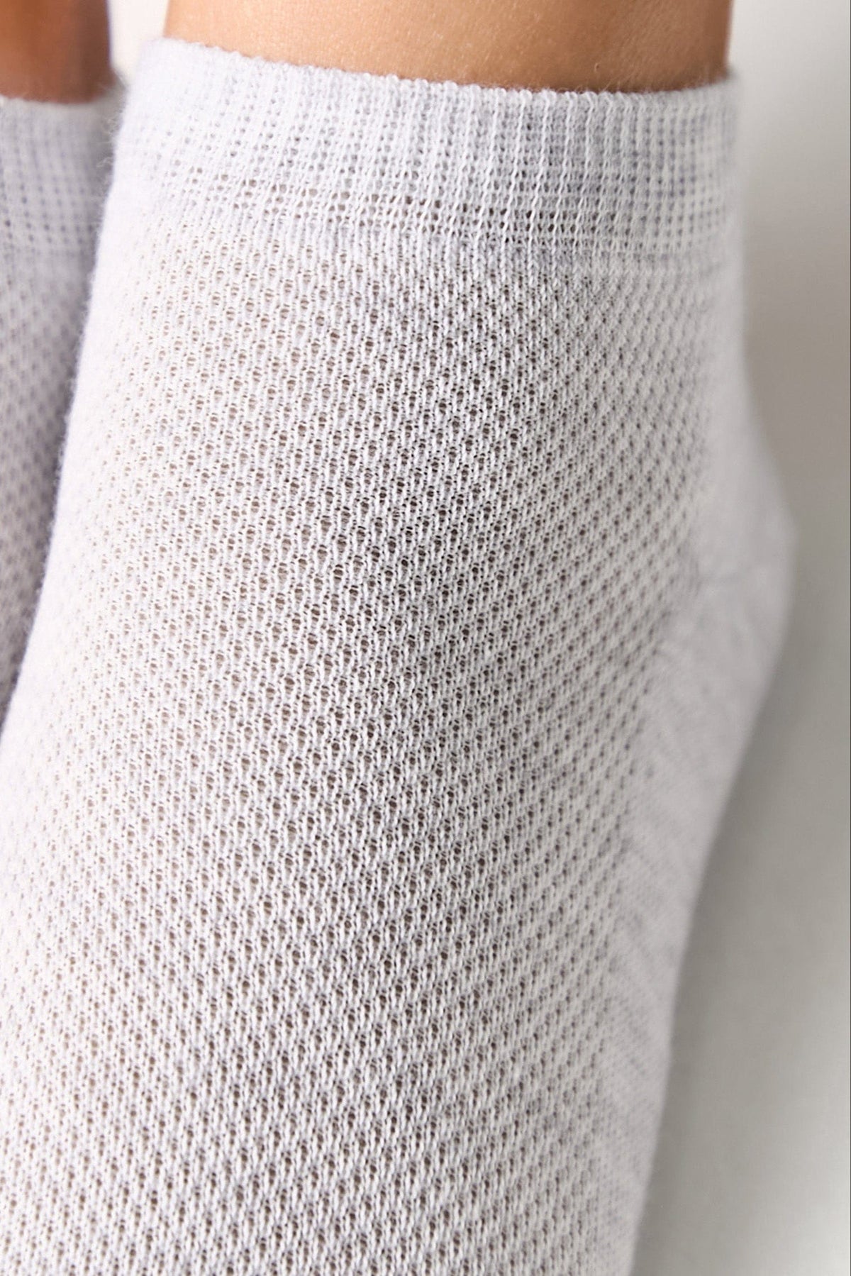 A close-up view of a white, textured fabric sock worn on a leg.