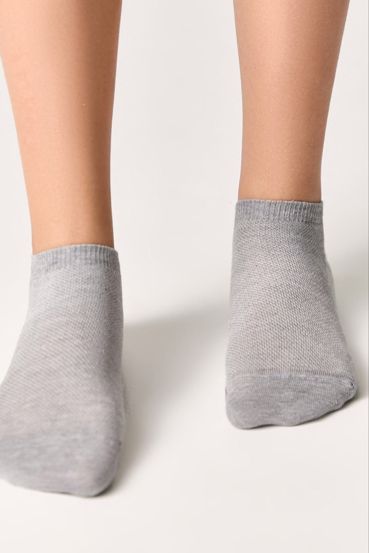 A pair of light grey ankle socks worn on feet against a plain white background.