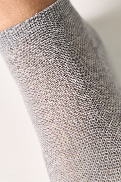 A close-up view of a light grey knitted sock being worn on a leg.
