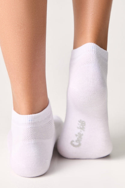 A pair of white ankle socks worn on the feet, featuring the brand name printed in light grey on the sole.