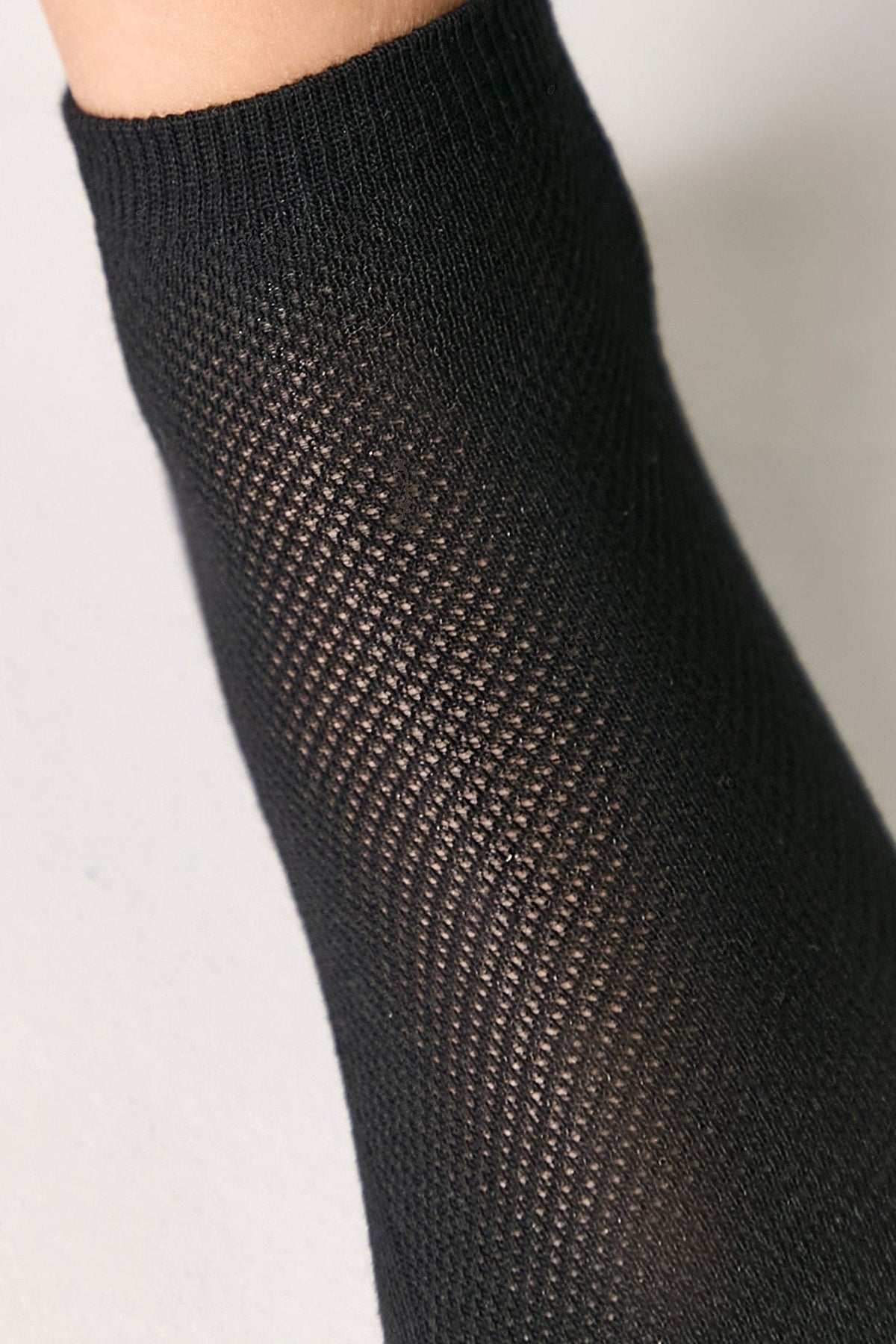 A close-up of a black textured sock showing a detailed diamond knit pattern worn on a person's leg.