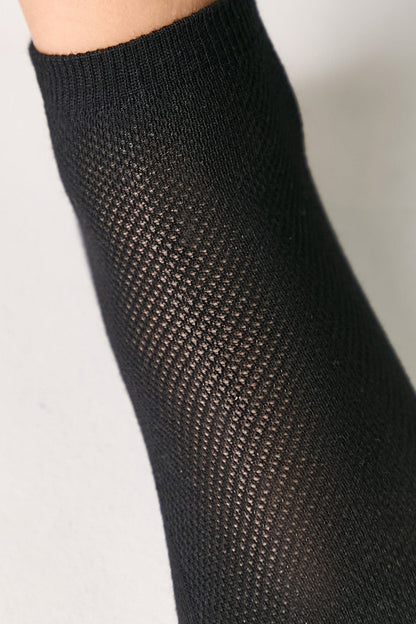A close-up of a black textured sock showing a detailed diamond knit pattern worn on a person's leg.