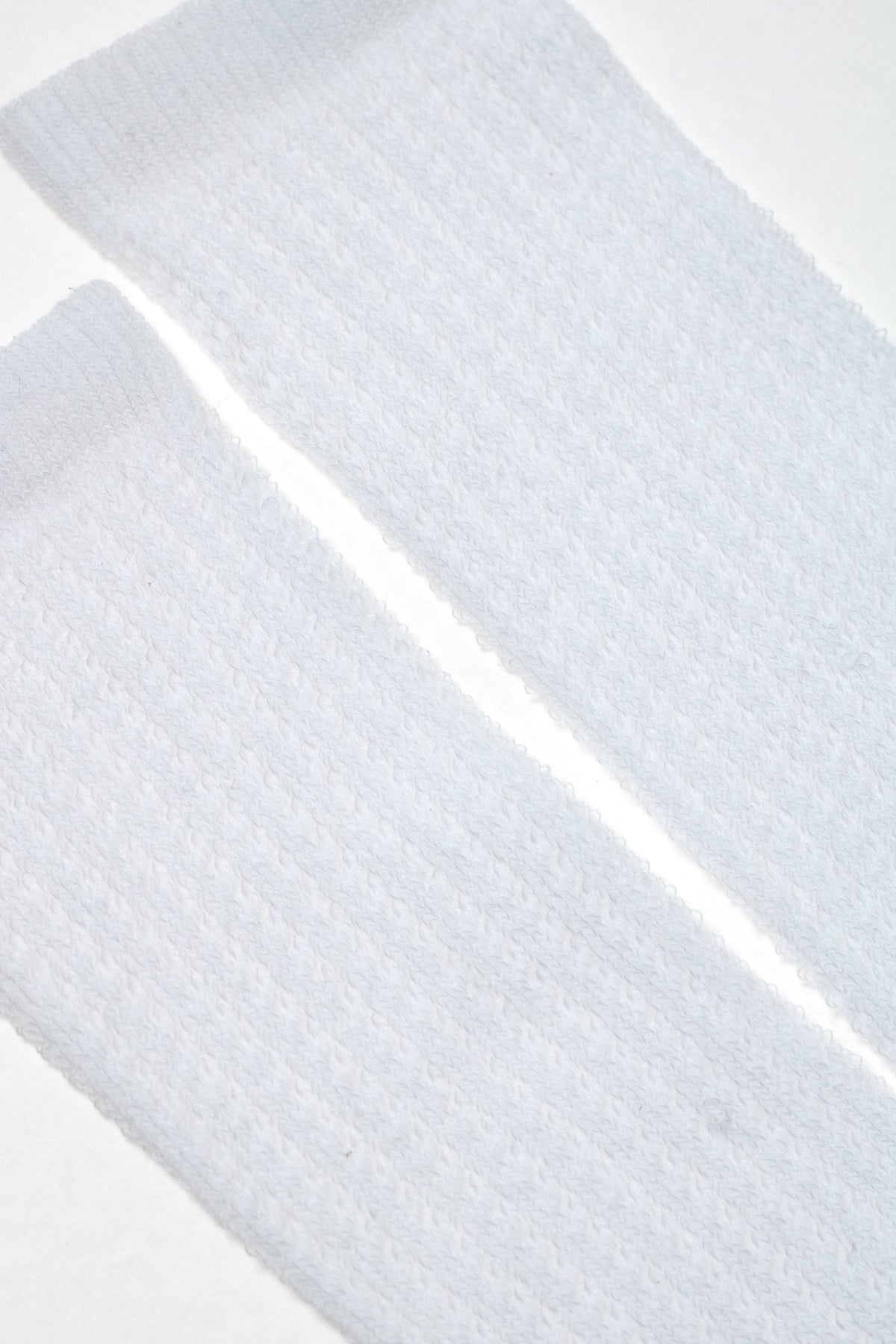 A pair of white textured mid-calf socks laid flat against a white background.
