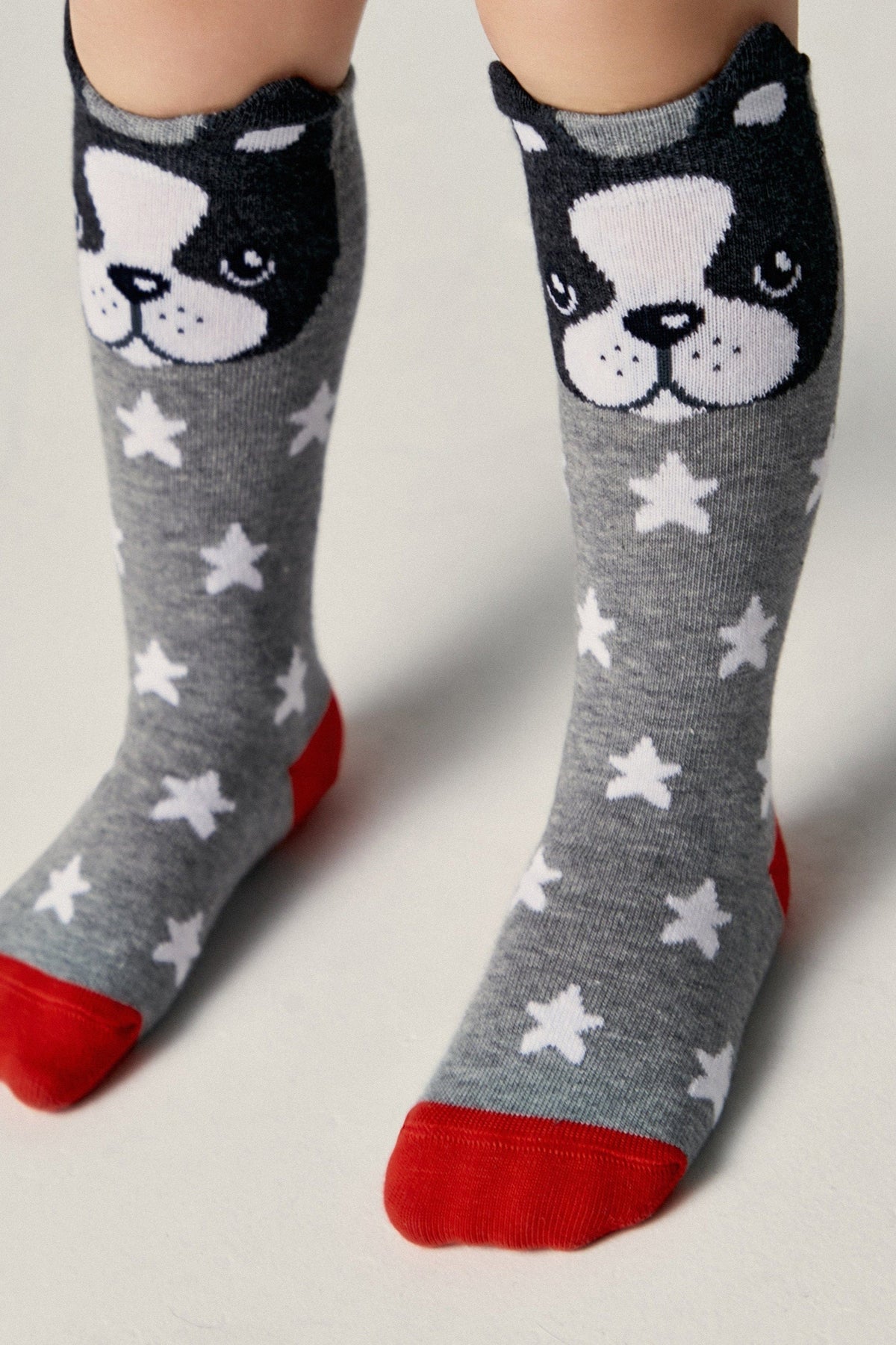 Grey knee-high socks featuring a white star pattern, red toes and heels, and a black and white French bulldog face design at the top.