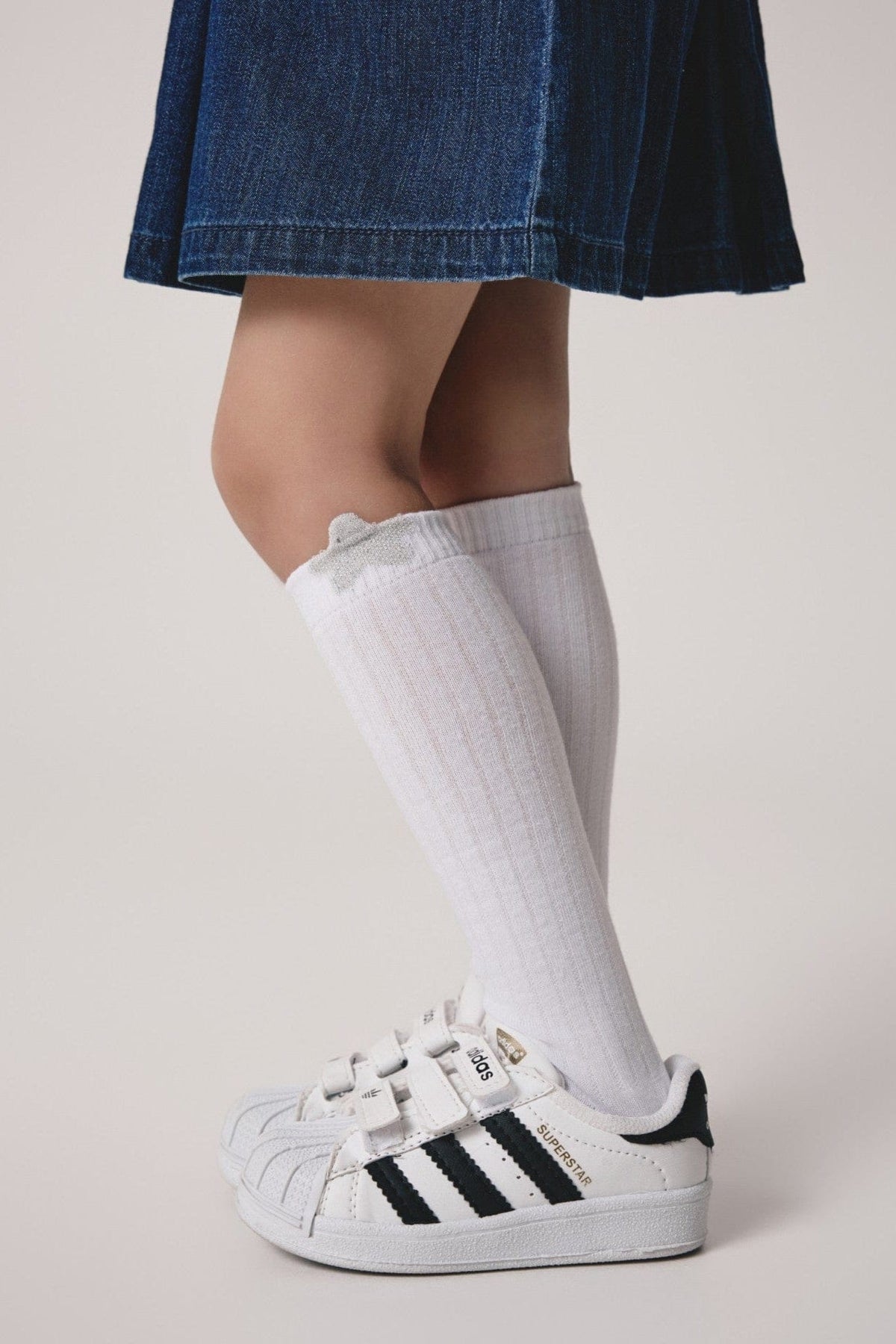 White mid-calf socks with a small grey star detail on the cuff worn with black and white velcro sneakers and a denim skirt.