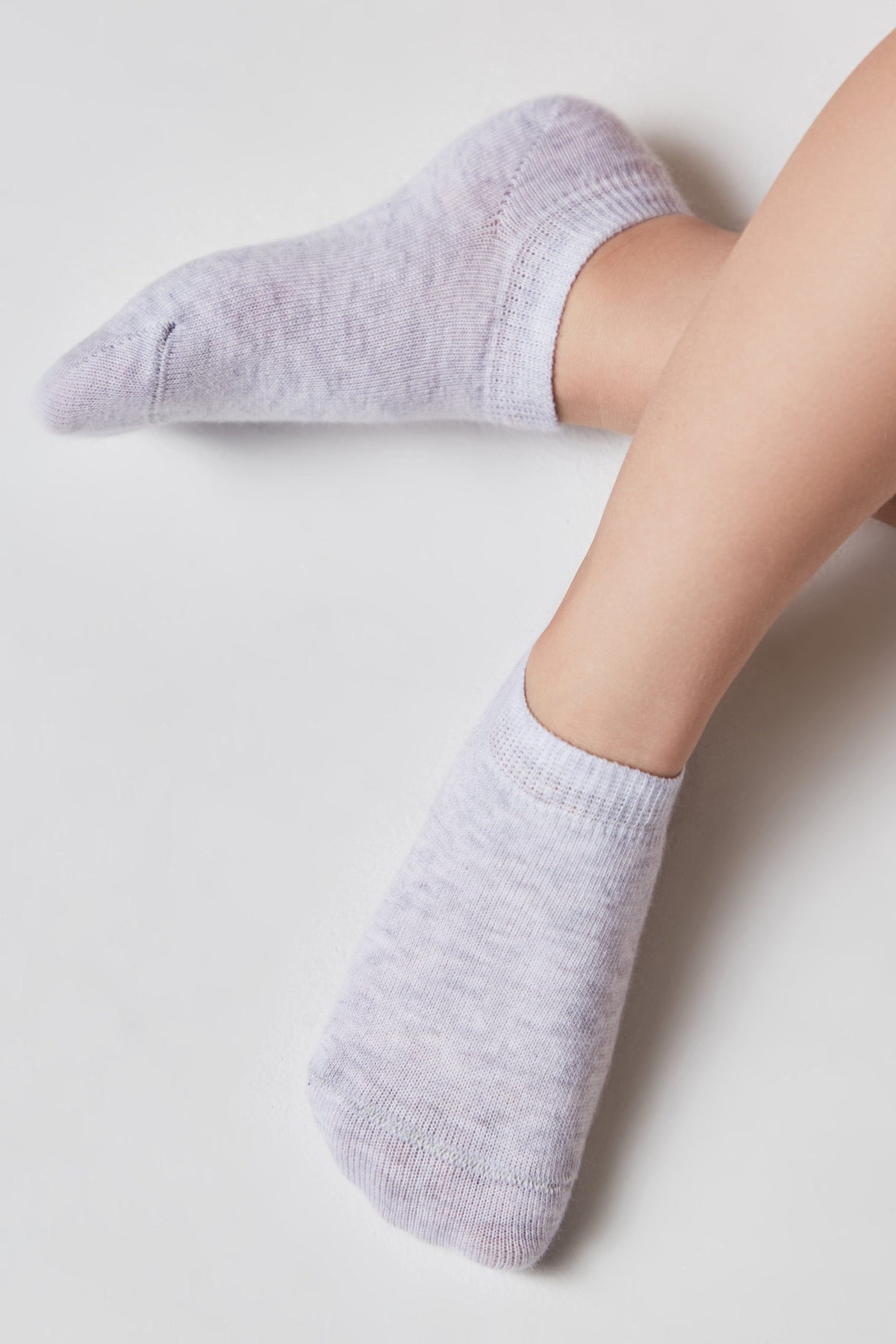 A pair of light heathered grey ankle socks worn on feet against a plain white background.