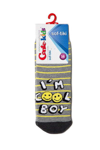 A grey children's sock with horizontal yellow stripes, featuring a graphic print that reads I'M COOL BOY with two yellow smiley face icons, attached to a branded cardboard retail hanger.