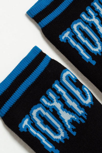 Two black socks feature a blue and light blue pixelated font that reads TOXIC, with blue and black striped cuffs.