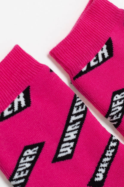 A close-up view of bright pink socks featuring a repeating black and white pattern of the word whatever inside a slanted rectangular block.