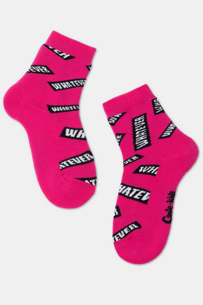 A pair of bright pink ankle socks patterned with repeated black and white rectangular speech bubbles containing the word "WHATEVER" printed in various orientations.
