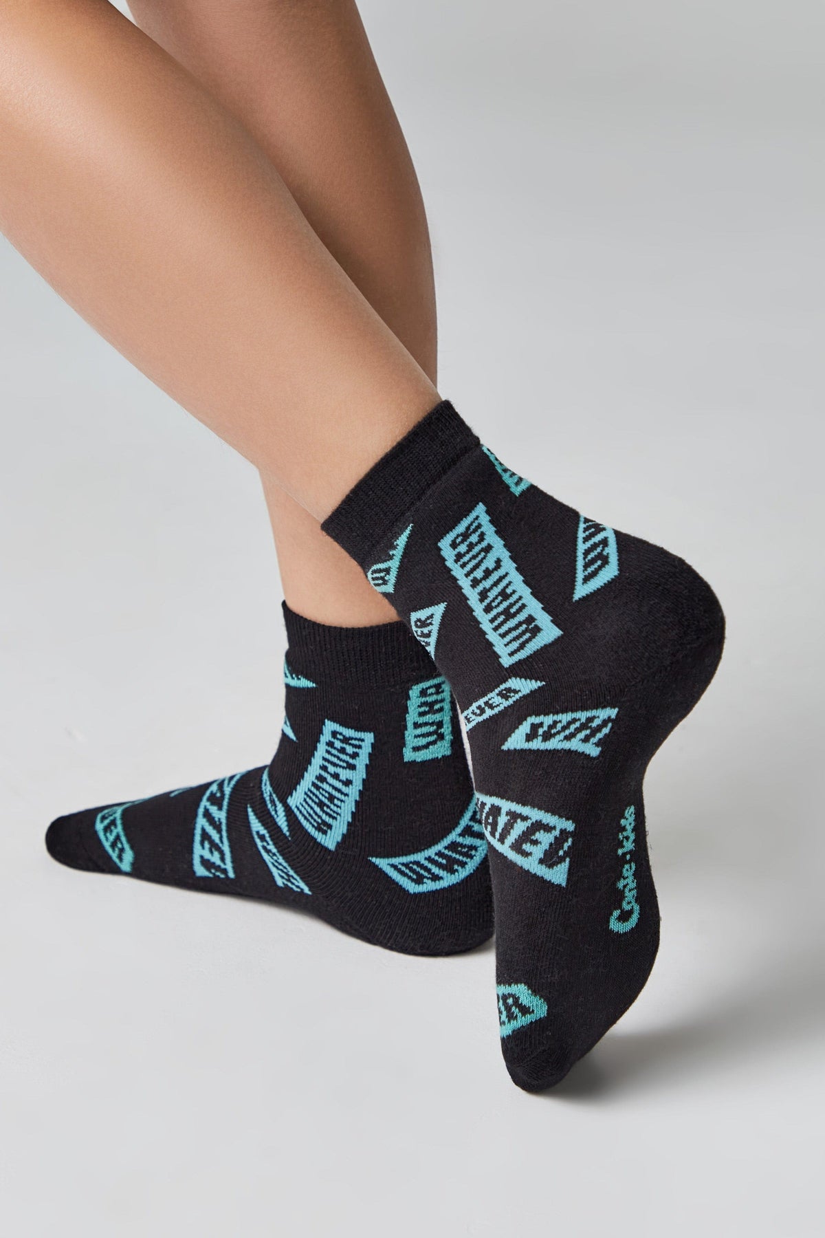 A person wears black ankle socks patterned with teal rectangular blocks containing the repeating text "WHATEVER".