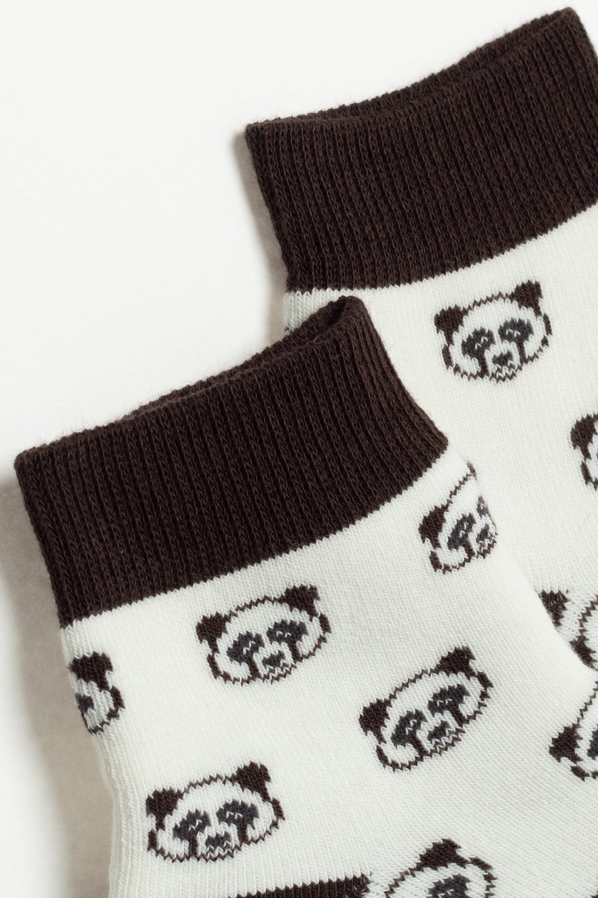 A pair of white socks with a dark brown ribbed cuff and a repeating pattern of small dark brown panda faces.