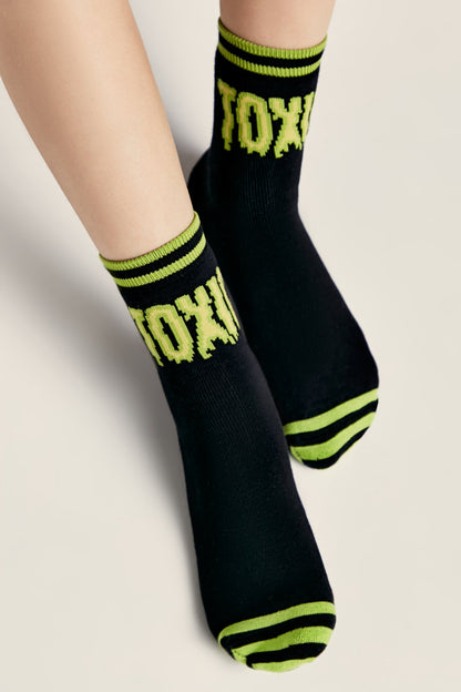 A pair of black ankle socks featuring the word TOXIC in a lime green pixelated font, accented with lime green striped detailing on the cuffs and toes.