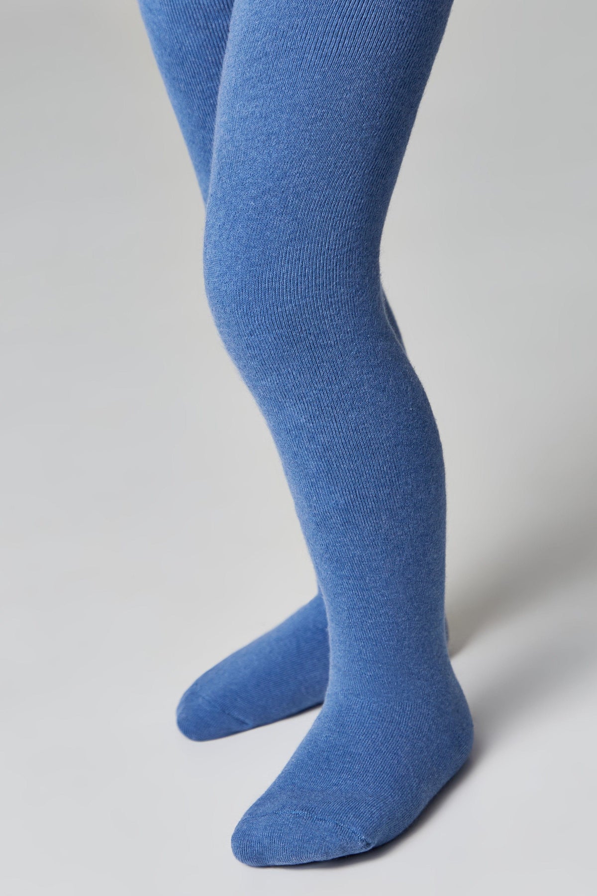 A pair of blue tights worn on a child's legs against a plain light gray background.