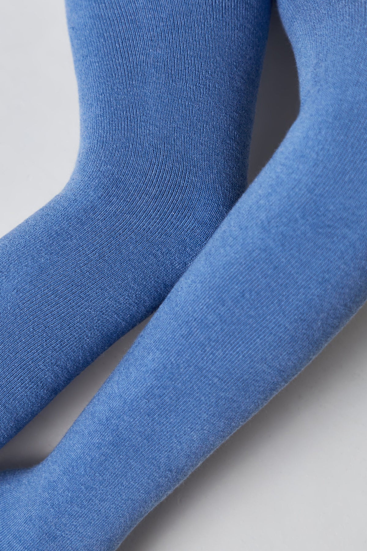 A close-up view of two blue fabric legs or sleeves positioned side-by-side against a plain white background.