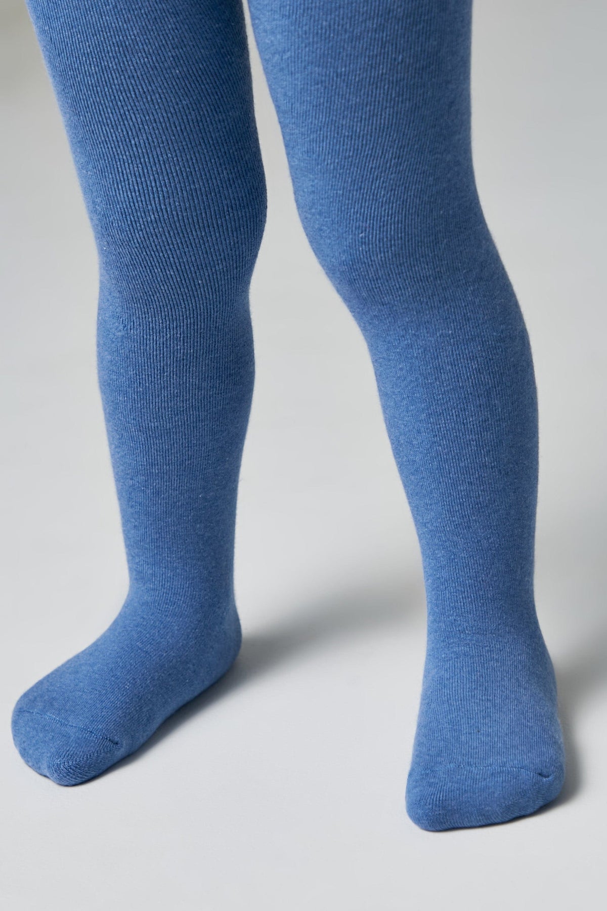 A pair of solid blue tights worn on a child's legs against a plain light gray background.