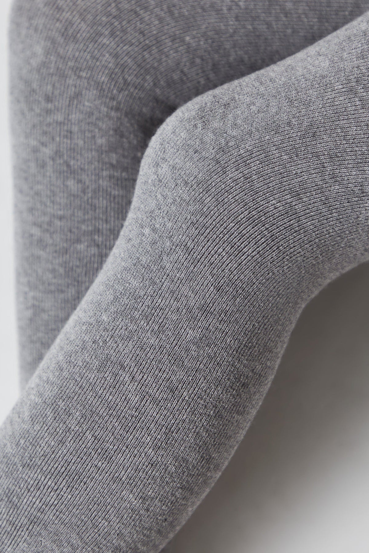 A close-up view of grey knit leggings worn on legs, showing the fine ribbed texture of the fabric.
