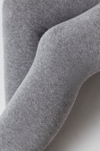 A close-up view of grey knit leggings worn on legs, showing the fine ribbed texture of the fabric.
