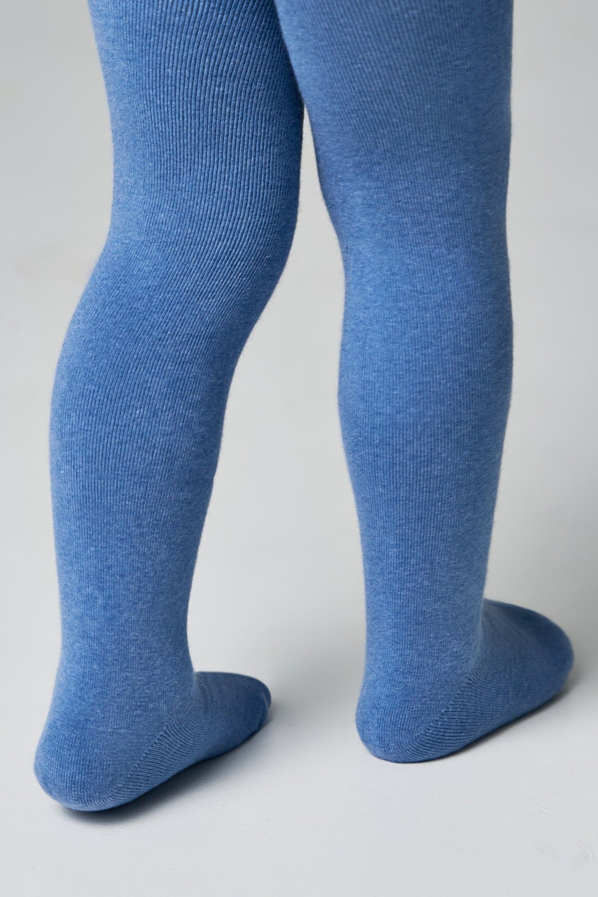 A pair of blue ribbed tights worn on a person's legs against a plain light gray background.