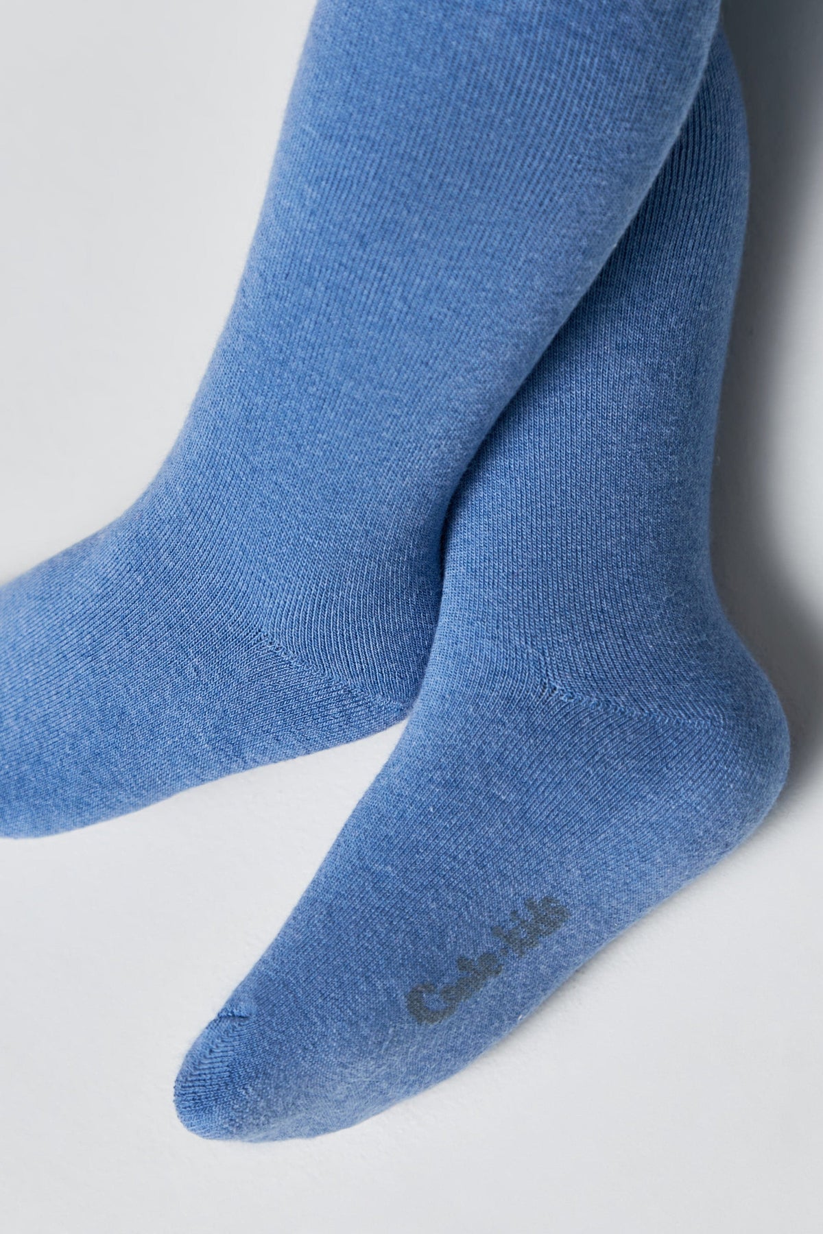 A pair of blue knit socks or tights for children, featuring a soft texture and a small logo printed on the heel.