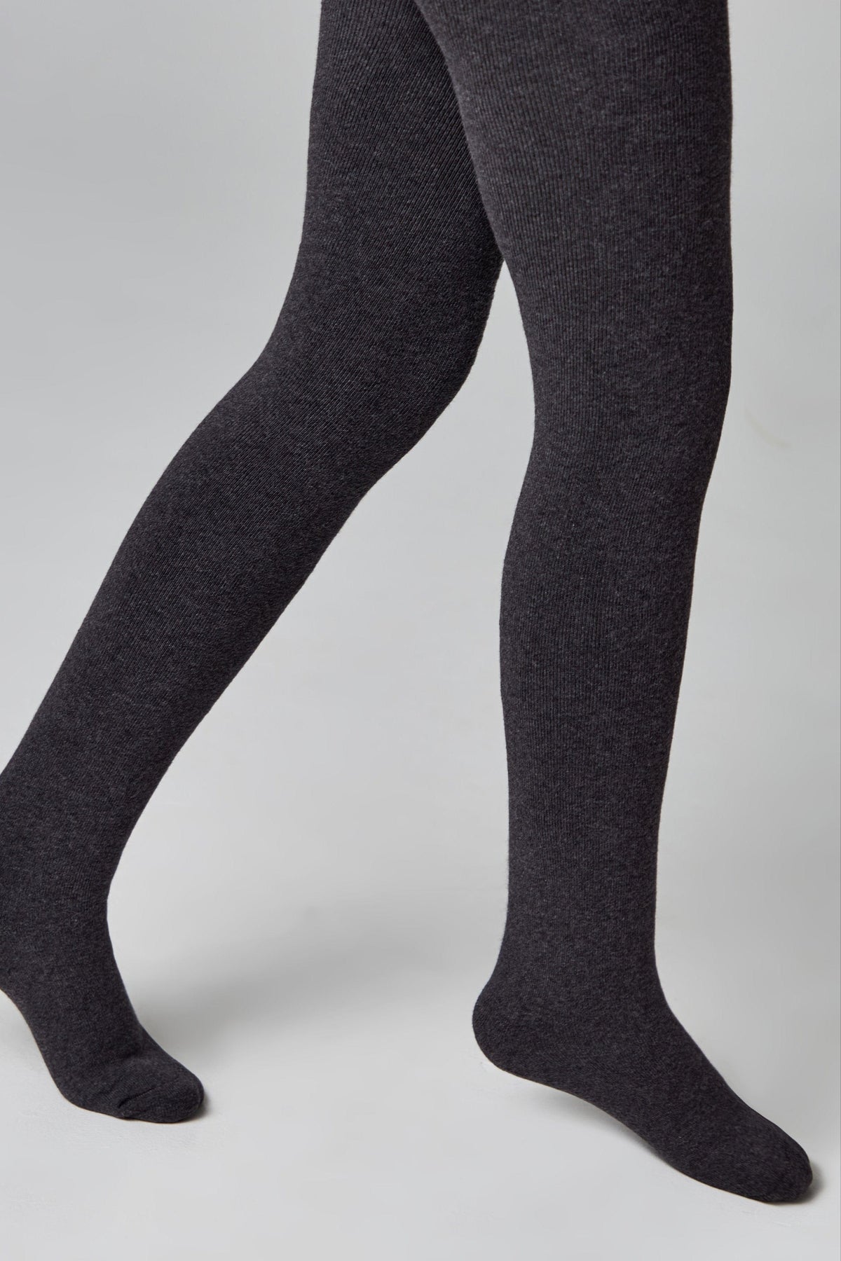 A pair of charcoal grey ribbed tights worn on a person's legs against a neutral grey background.