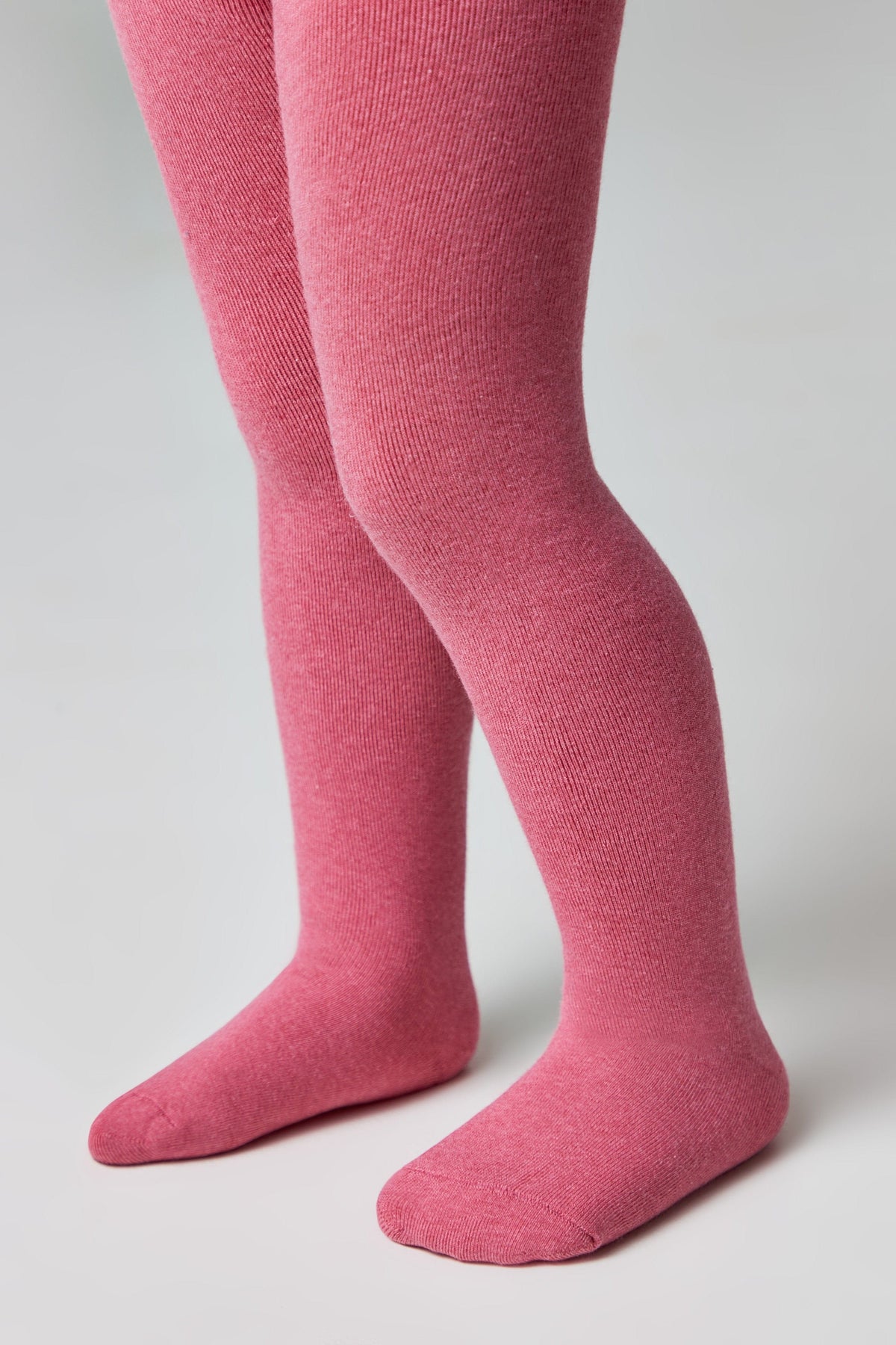 A pair of pink knitted tights worn on a child's legs against a plain light grey background.
