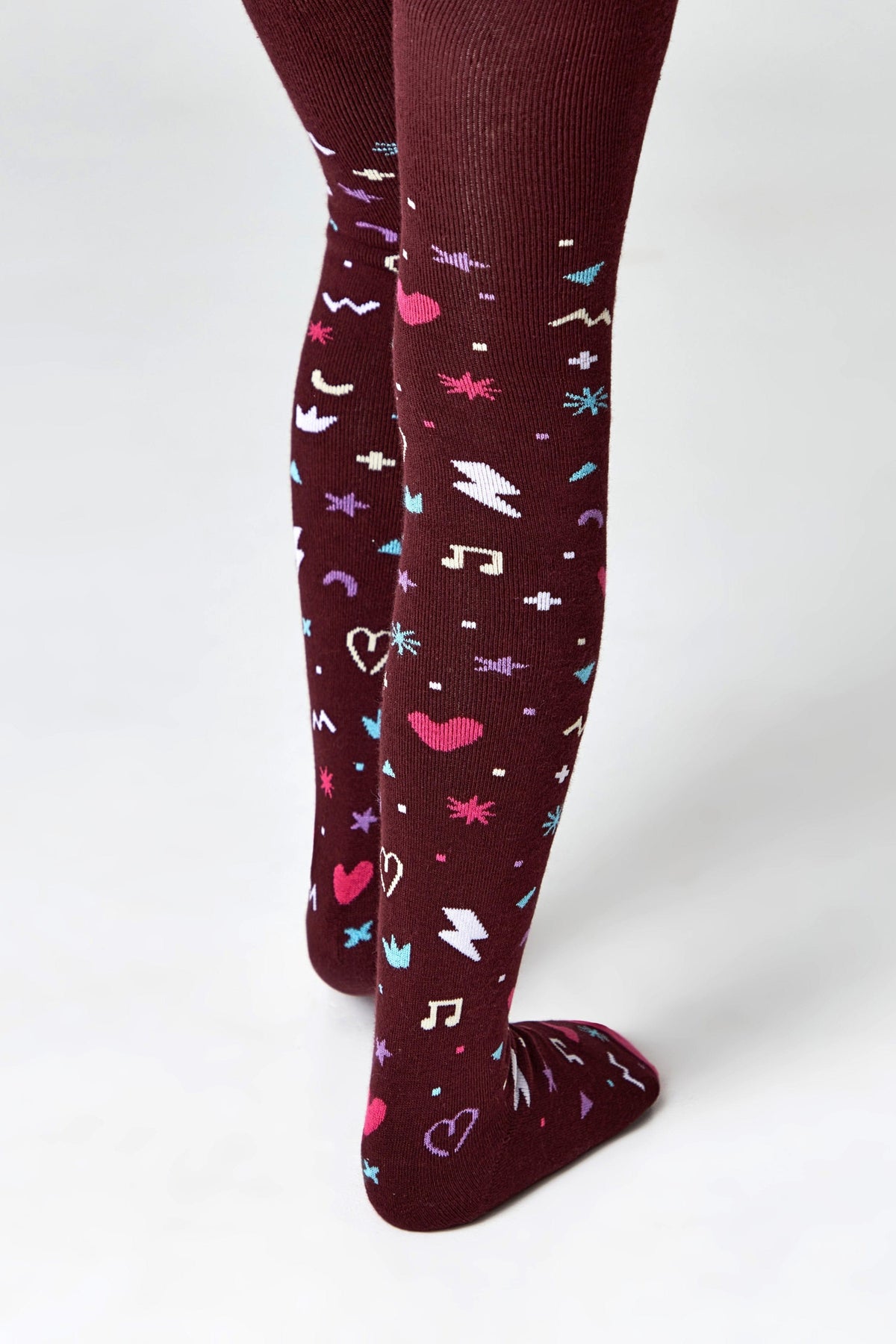 Maroon tights featuring a repeating pattern of white, blue, and pink graphic icons including hearts, musical notes, and lightning bolts.