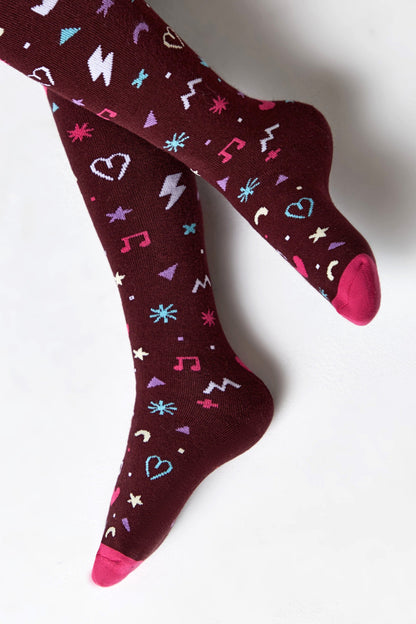 A pair of maroon knee-high socks featuring a repeated pattern of pink, blue, and white icons including hearts, music notes, lightning bolts, and stars with pink toes and heels.