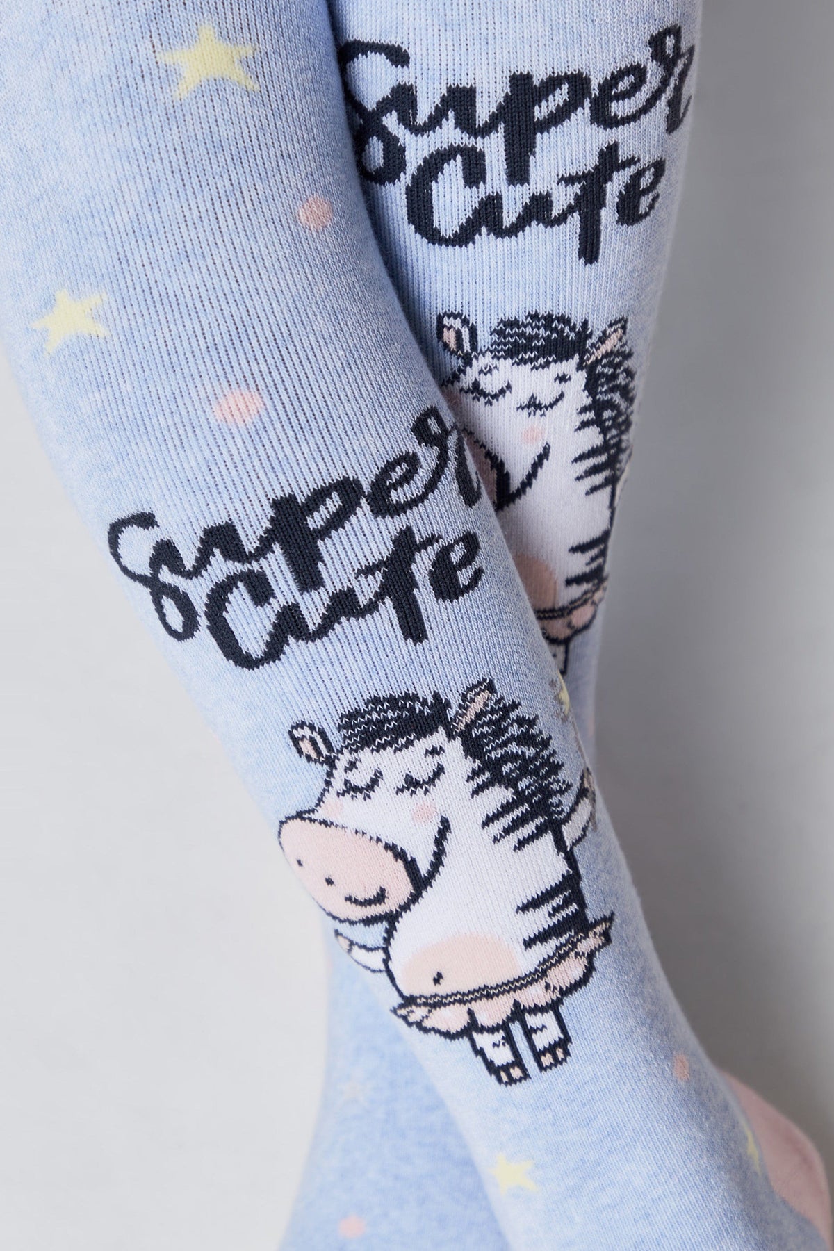 A pair of light blue children's tights featuring a repeating pattern of cartoon zebras, yellow stars, and the words Super Cute in black script.
