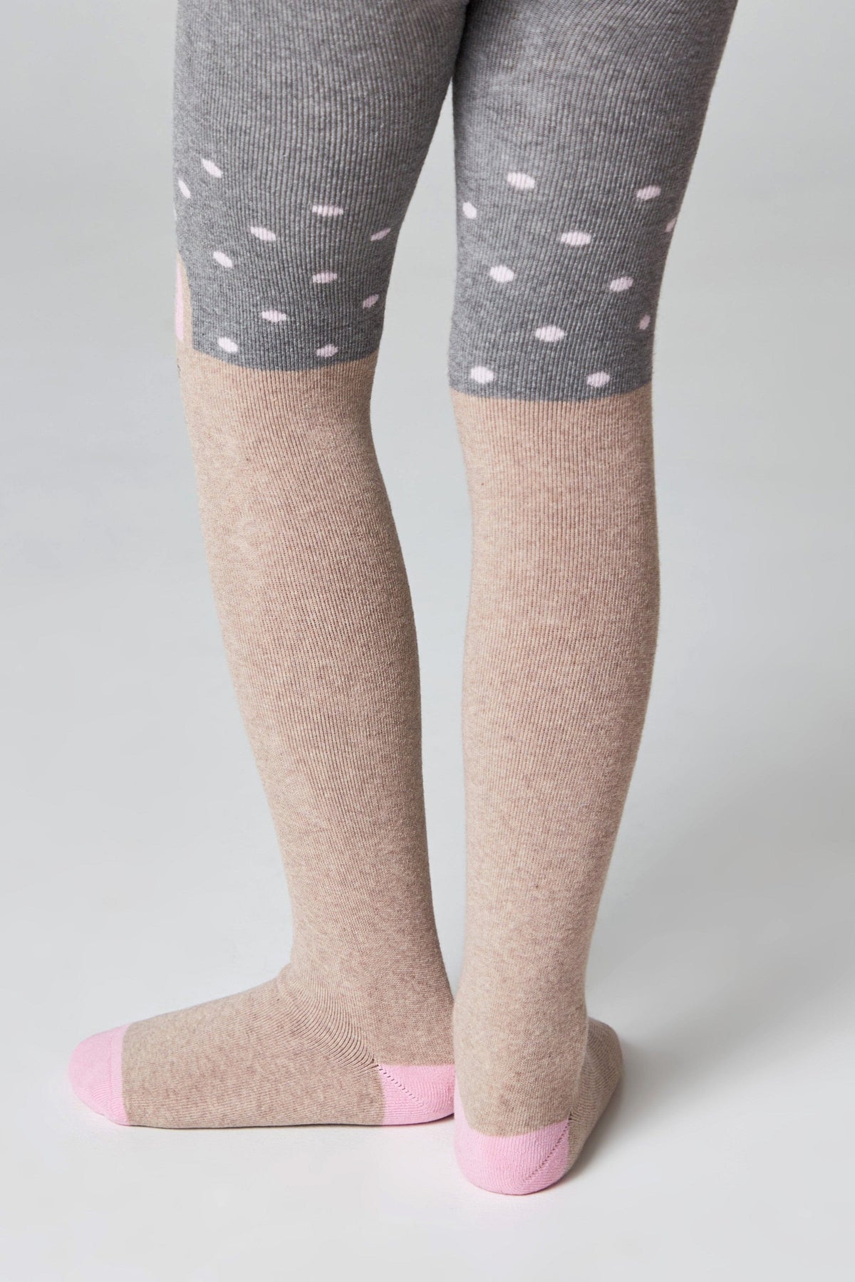 Children's tights featuring a gray upper section with white polka dots and a tan lower section with solid pink heels and toes.
