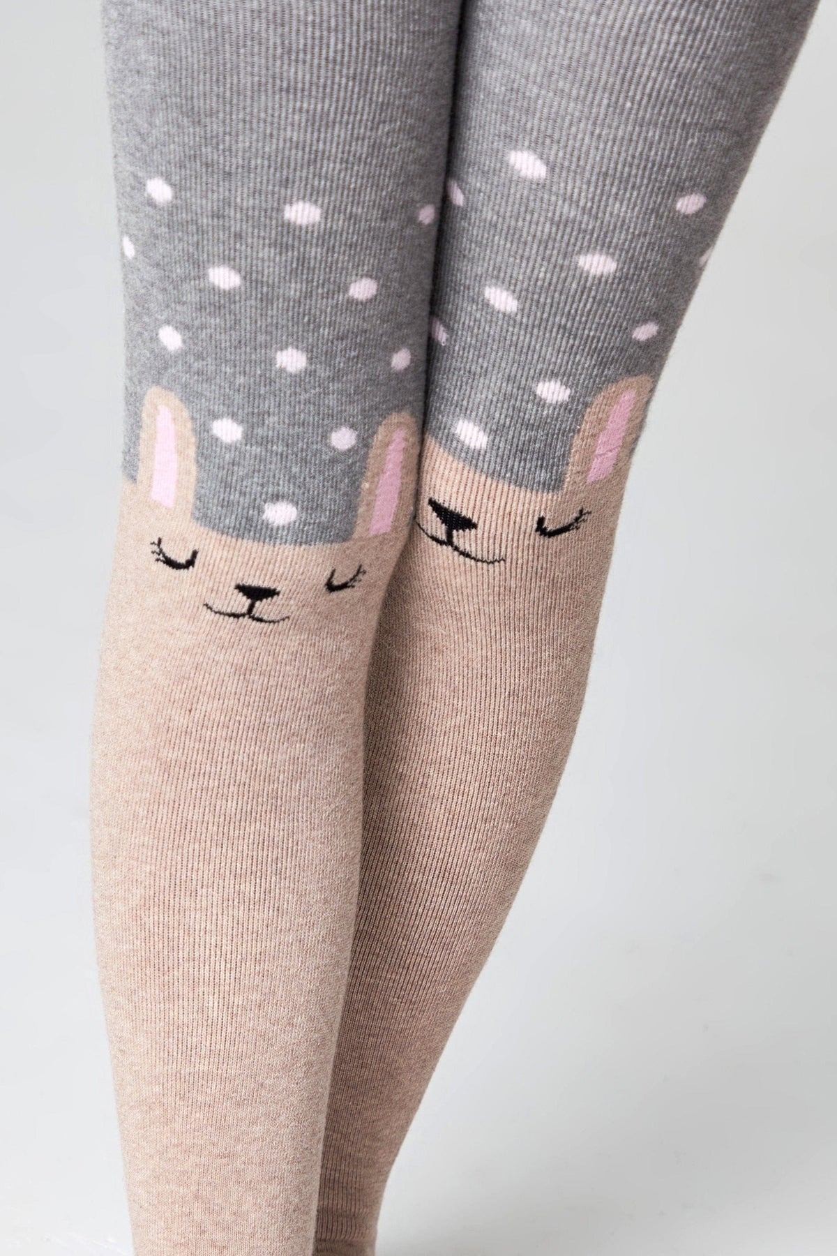 Children's tights featuring a grey polka dot pattern on the thighs and a beige lower section with a cute, sleepy-faced bunny character design on each knee.