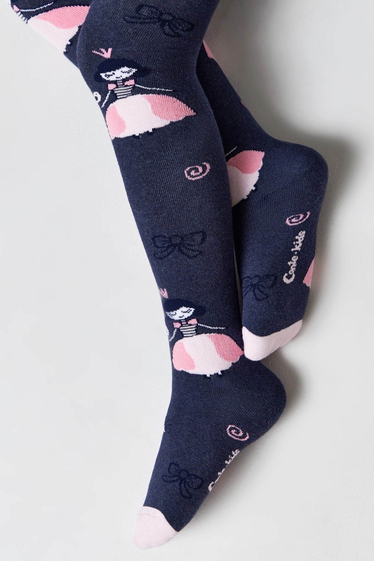 Children's tights in a dark blue hue featuring a repeating pattern of cartoon ballerinas with pink dresses, small bows, and swirl accents, with pink detailing on the toes and heels.