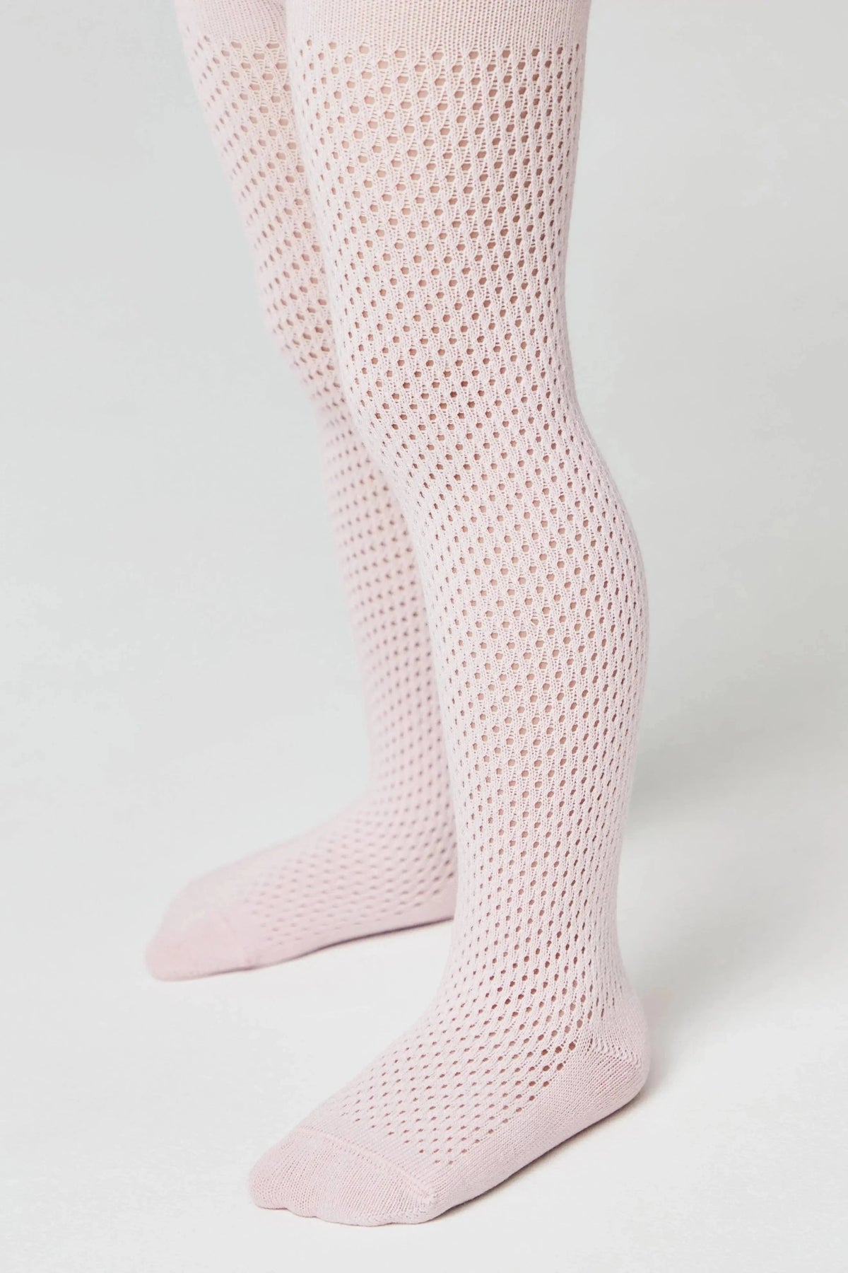 A pair of light pink tights with a textured, open-knit honeycomb pattern on the legs and solid fabric at the toes and heels, shown on a child's legs against a plain white background.