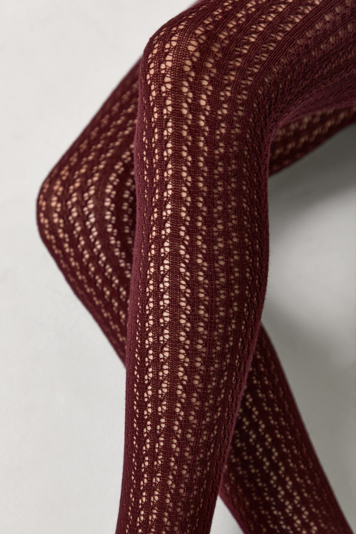 Burgundy tights featuring a delicate openwork vertical knit pattern on the legs.