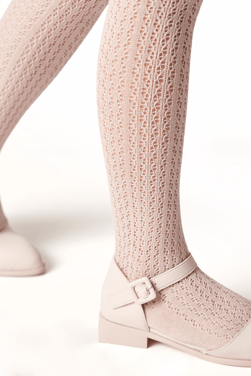 A pair of pale pink textured knit tights paired with matching buckled Mary Jane shoes on a white background.