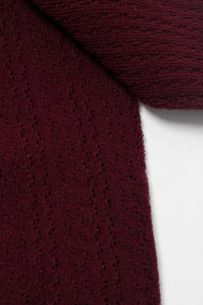 A close-up of a burgundy knit fabric featuring vertical, eyelet lace-style detailing against a white background.