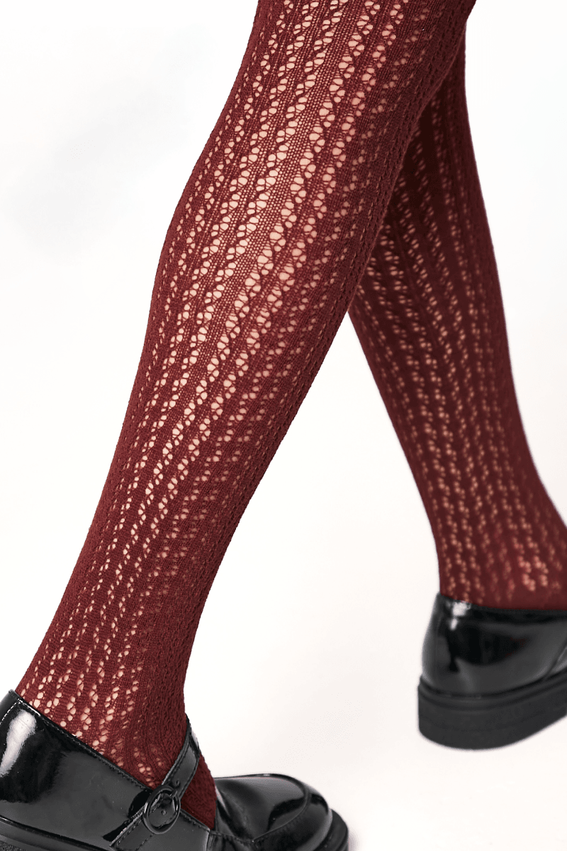 Burgundy knit tights with an intricate openwork pattern worn with glossy black Mary Jane shoes.