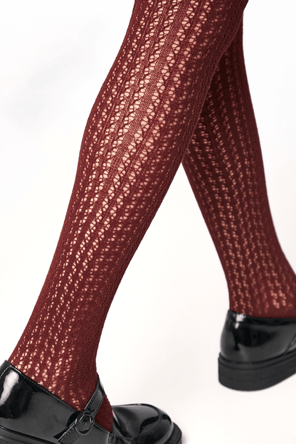 Burgundy knit tights with an intricate openwork pattern worn with glossy black Mary Jane shoes.