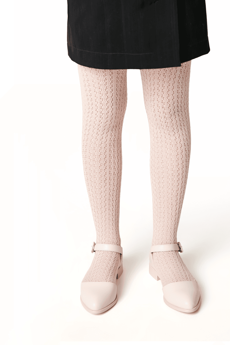 A pair of pale pink textured knit tights worn with matching pointed-toe flat shoes featuring an ankle strap and a black skirt.