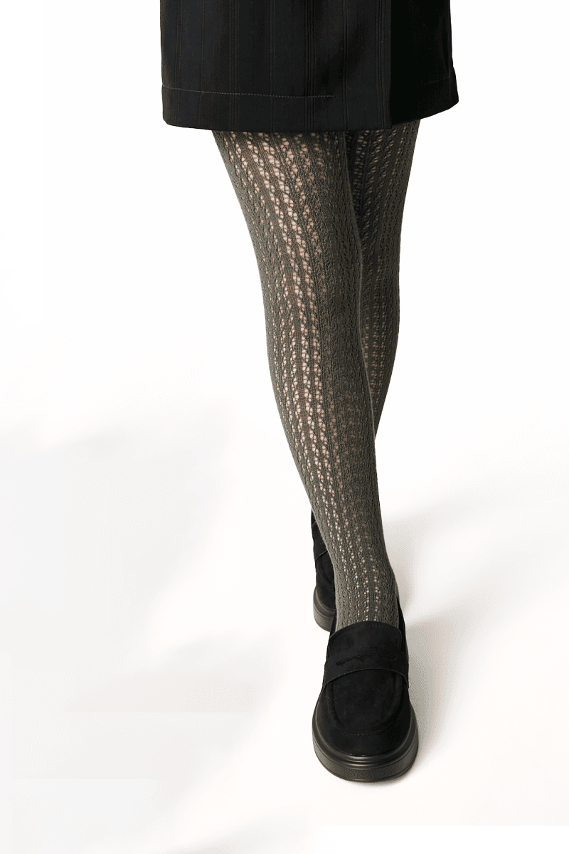 A person wears olive green cable-knit tights with a black skirt and black slip-on shoes.