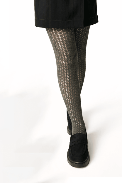 A person wears olive green cable-knit tights with a black skirt and black slip-on shoes.